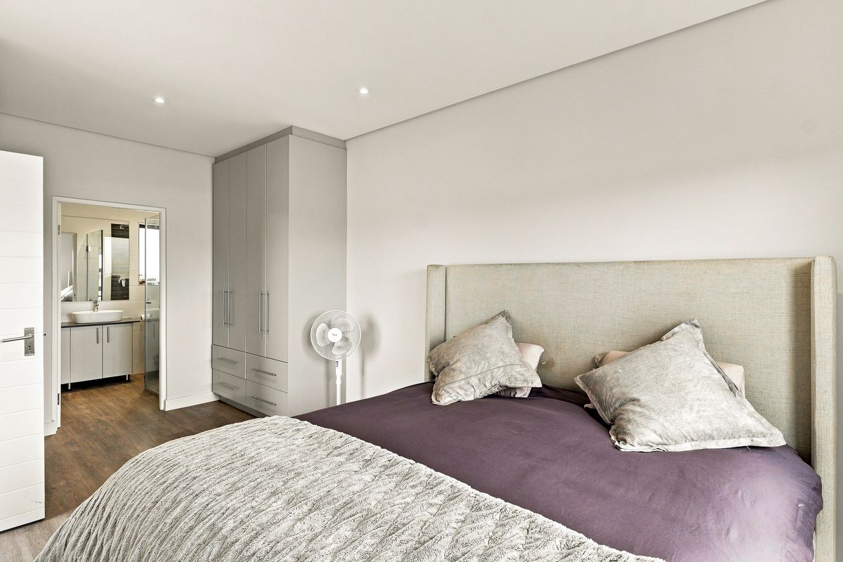 A well-maintained bedroom featuring built-in cupboards, recessed lighting, and laminate flooring, with direct access to an en-suite bathroom.