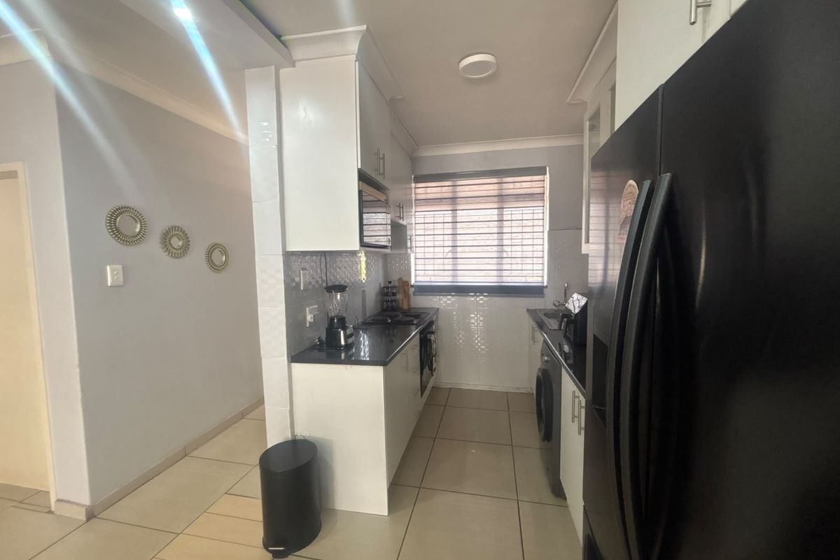 A functional kitchen featuring white cabinetry, dark granite countertops, built-in oven and hob, and tiled flooring with a window for natural light.