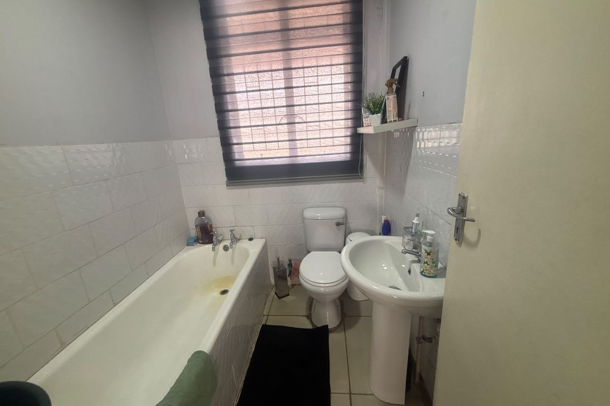 A functional bathroom featuring a pedestal basin, toilet, and bathtub with tiled finishes, requiring minor cosmetic updates to improve its overall condition.