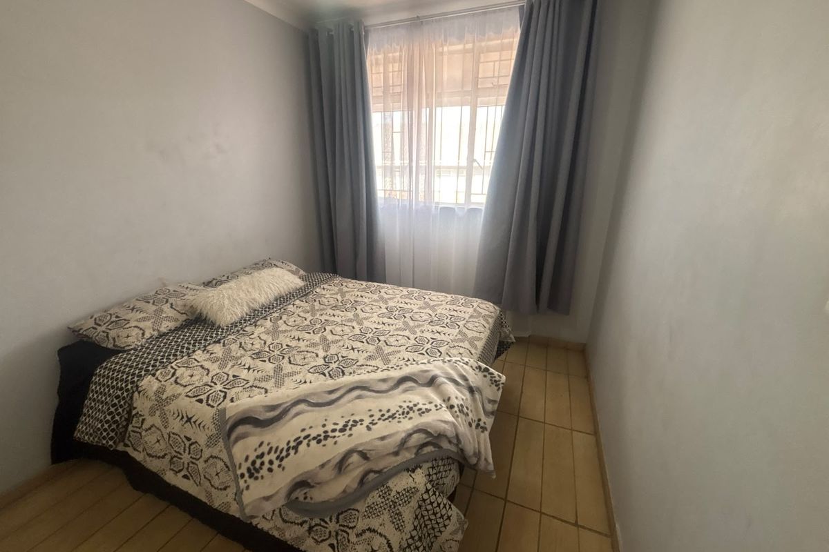 A compact bedroom featuring tiled flooring, neutral wall finishes, and a window fitted with security bars.