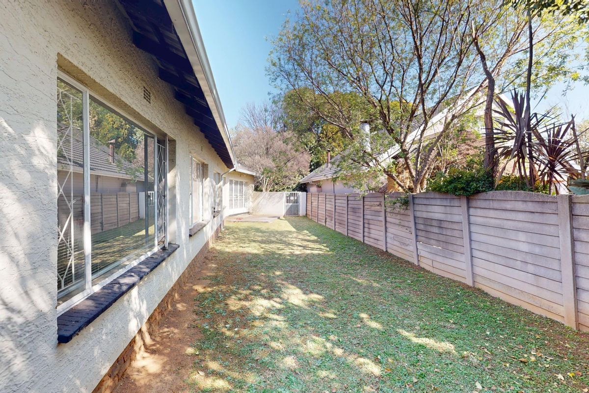 A side garden area featuring a precast concrete boundary wall, security-barred windows, and established trees along the rear perimeter of the property.