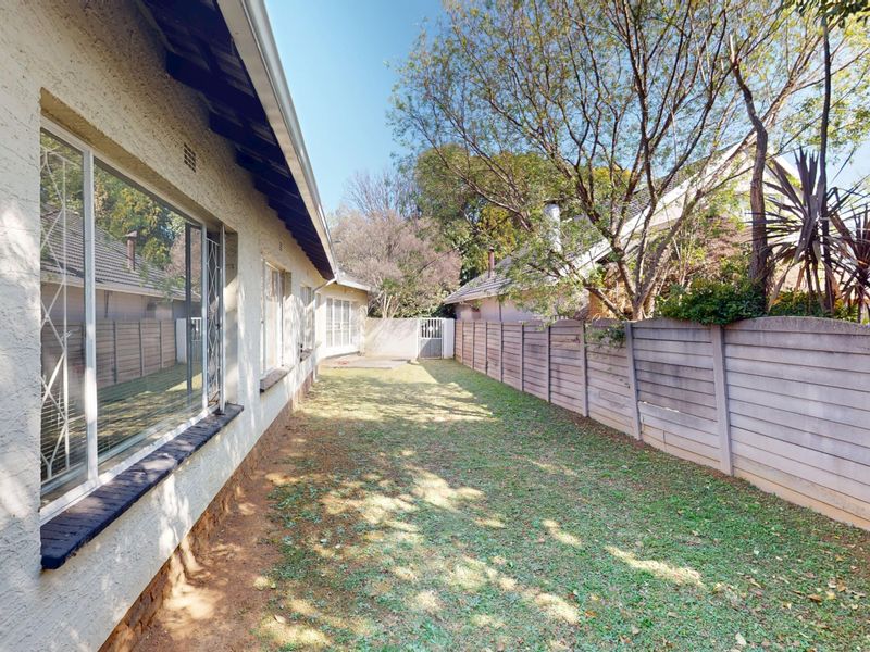 A side garden area featuring a precast concrete boundary wall, security-barred windows, and established trees along the rear perimeter of the property.