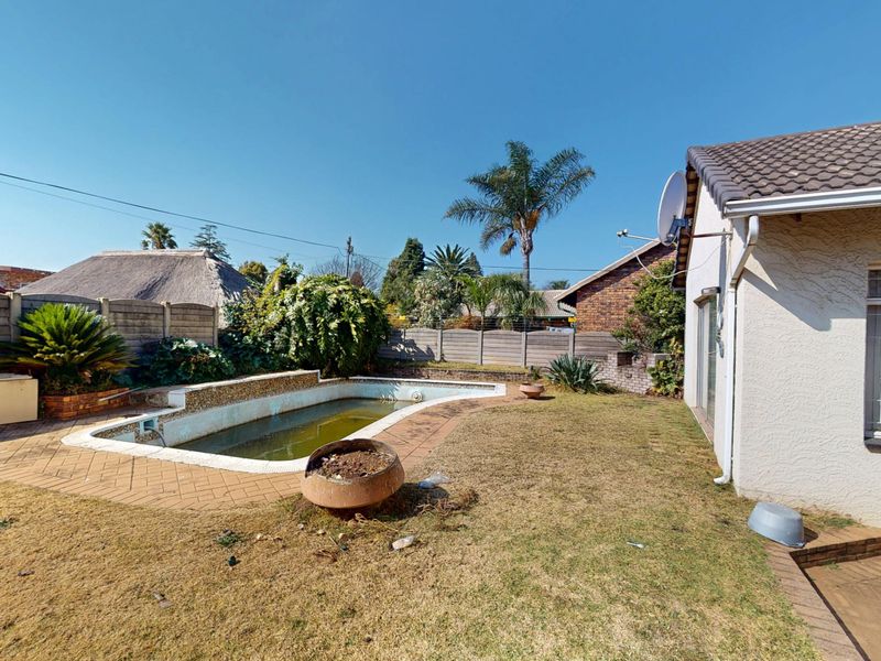 Rear garden area featuring a swimming pool with paved surround, enclosed by precast concrete boundary walls and adjacent to the main house structure.