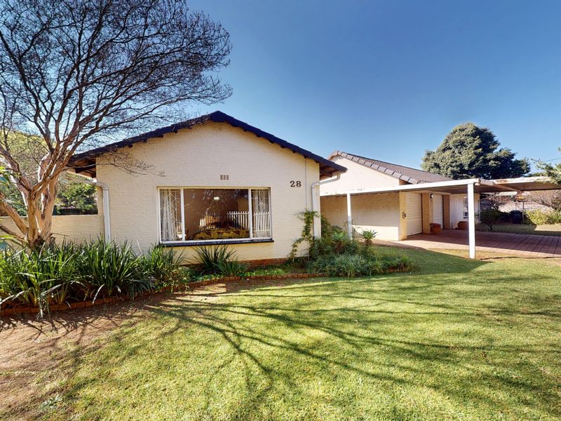 Front view of a single-story house featuring a paved driveway, carport, and a well-maintained front garden.