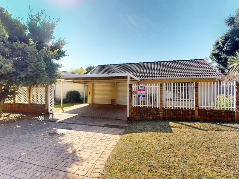 Front view of the property featuring a paved driveway, double carport, and secure perimeter fencing with a brick boundary wall.
