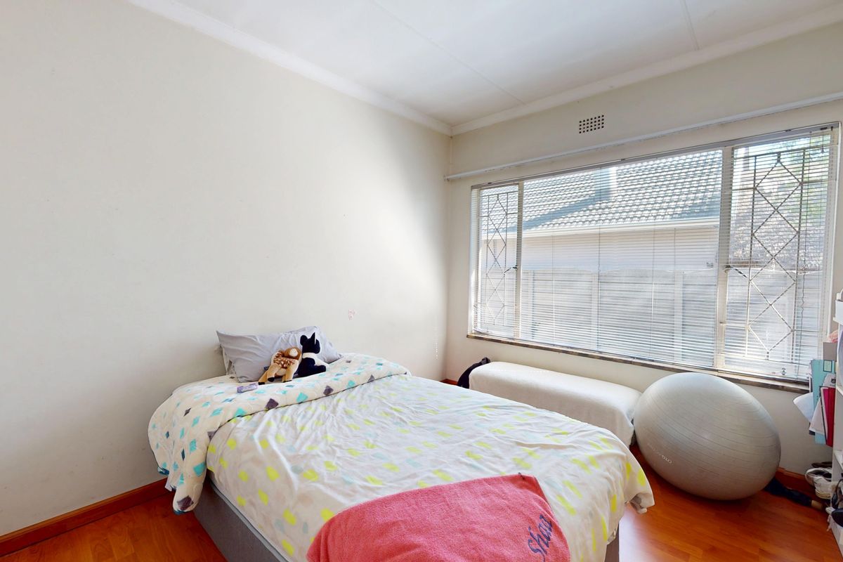 A bright bedroom featuring laminate flooring, a large window with security bars, and neutral wall finishes.