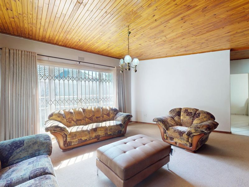 Spacious living room featuring a timber tongue and groove ceiling, brick fireplace, and large windows with security gates.