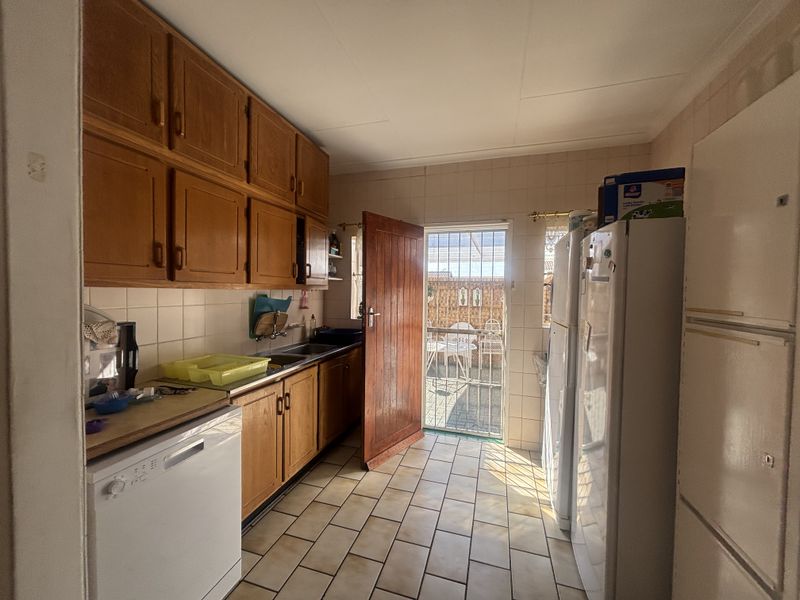 A functional scullery area featuring built-in wooden cabinetry, tiled flooring, and direct access to the rear patio through a security gate.