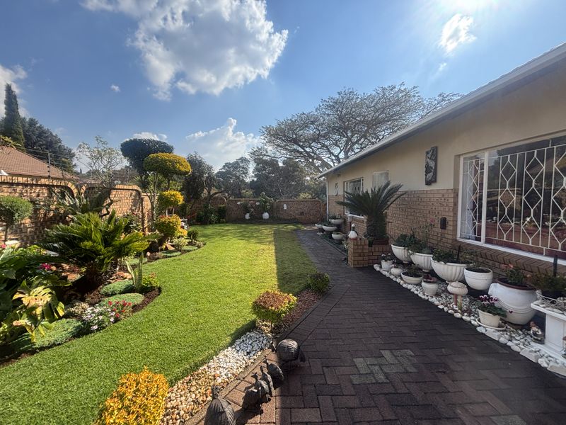 A well-maintained rear garden featuring a paved walkway, manicured lawn, and established landscaping enclosed by a brick boundary wall.