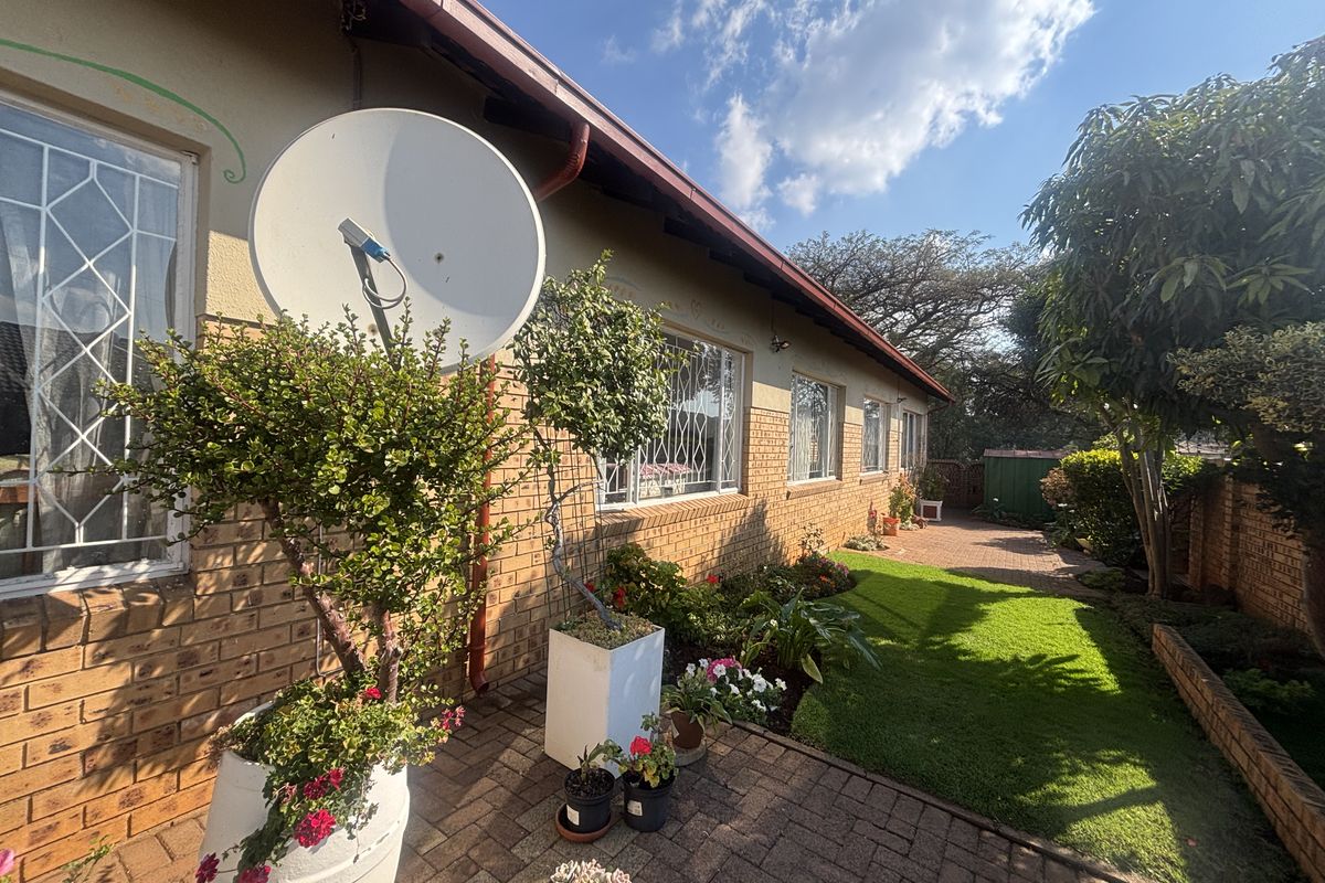 A well-maintained rear exterior view featuring a brick facade, paved patio area, and established garden space.