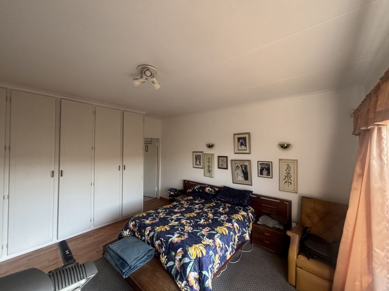 A bedroom featuring built-in cupboards, wall-mounted lighting, and wood-look flooring.