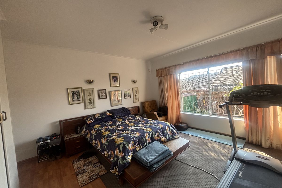 Spacious bedroom featuring laminate flooring, a built-in headboard, and large windows fitted with security bars for added protection.