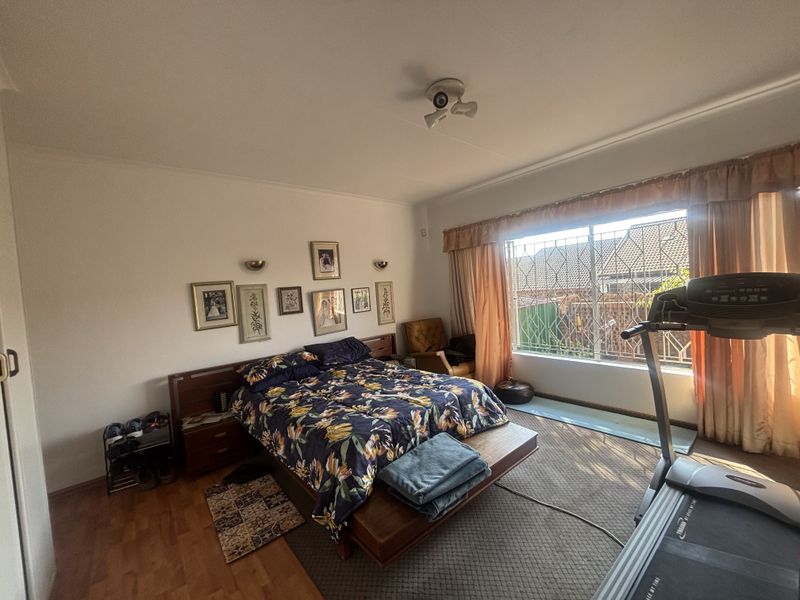 Spacious bedroom featuring laminate flooring, a built-in headboard, and large windows fitted with security bars for added protection.