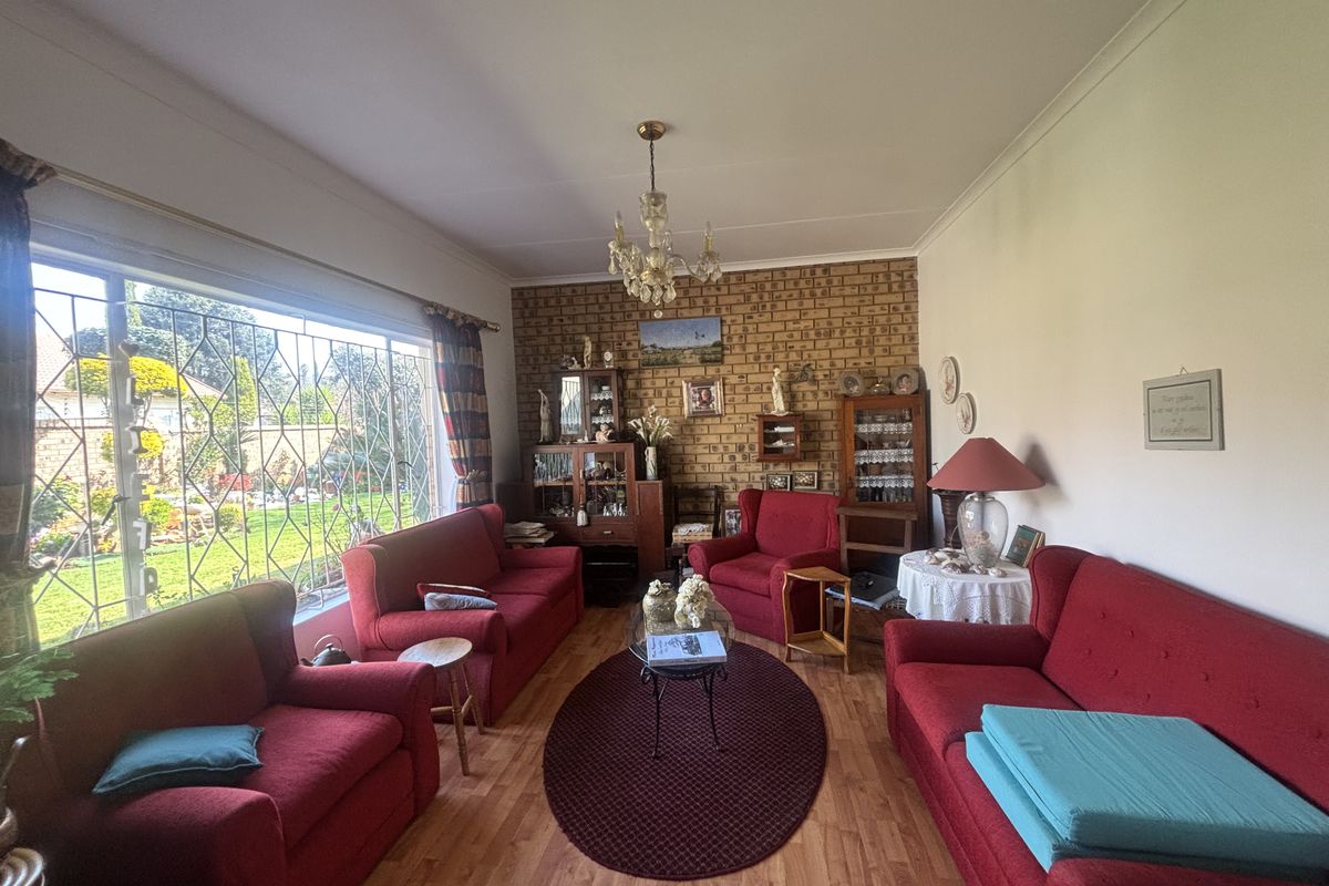 A spacious living room featuring an exposed brick accent wall, laminate flooring, and a large window overlooking the garden.