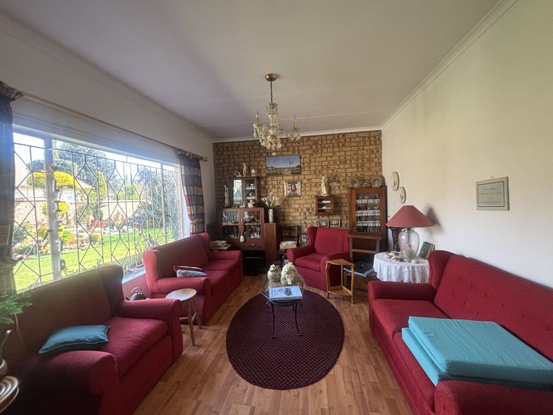 A spacious living room featuring an exposed brick accent wall, laminate flooring, and a large window overlooking the garden.
