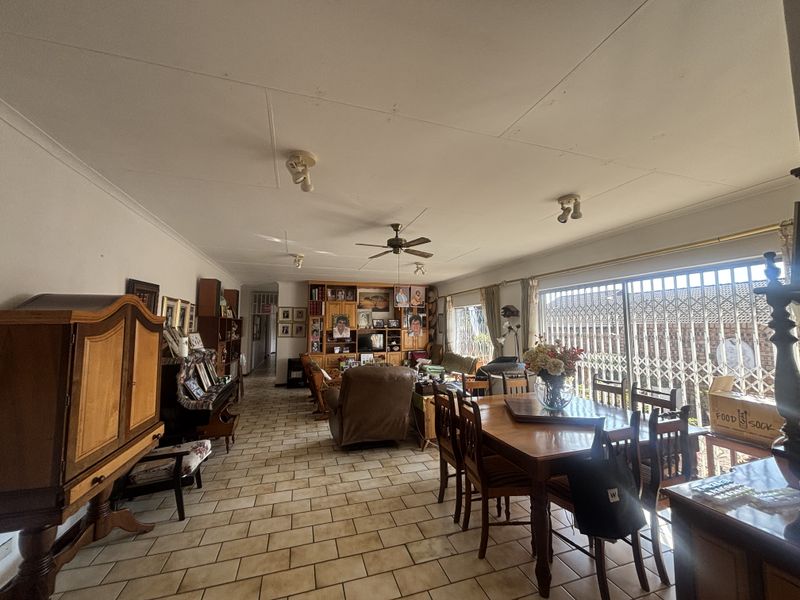 Spacious open-plan living and dining area featuring ceramic tile flooring, a ceiling fan, and large sliding doors with security gates leading to the exterior.
