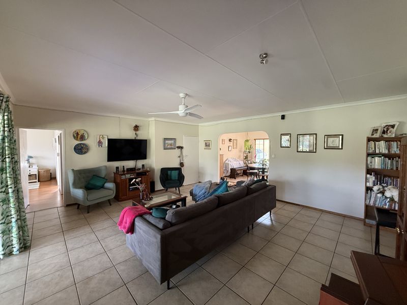 Spacious living room featuring neutral tiled flooring, a ceiling fan, and an open archway leading to an adjacent dining area.