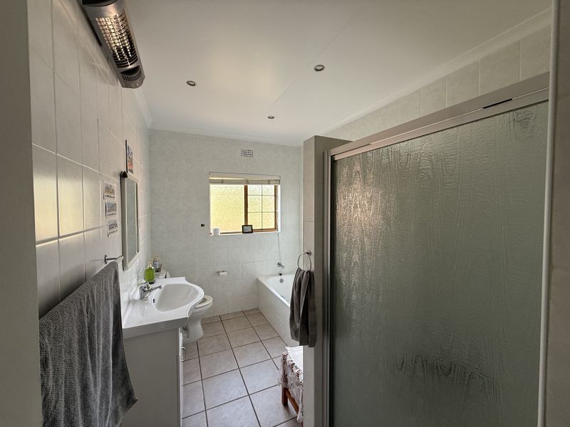 A functional bathroom featuring a shower enclosure, bathtub, and pedestal basin with neutral wall and floor tiling.