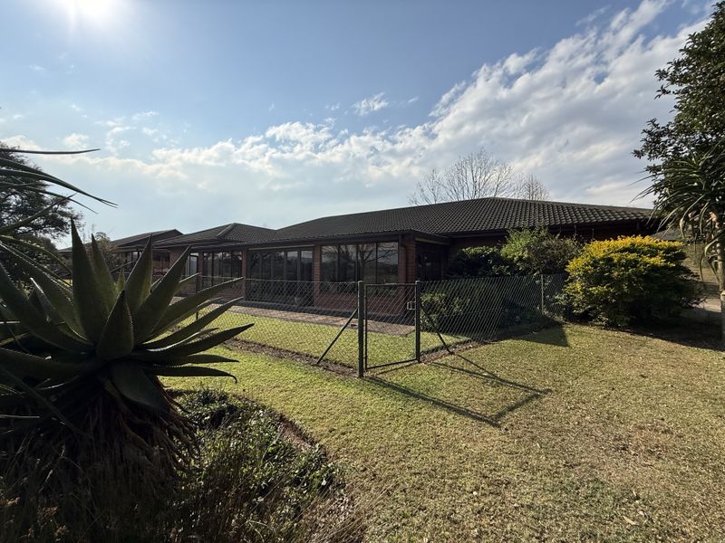 Rear view of the property featuring a brick facade, tiled roof, and a paved patio area accessible through large sliding glass doors.