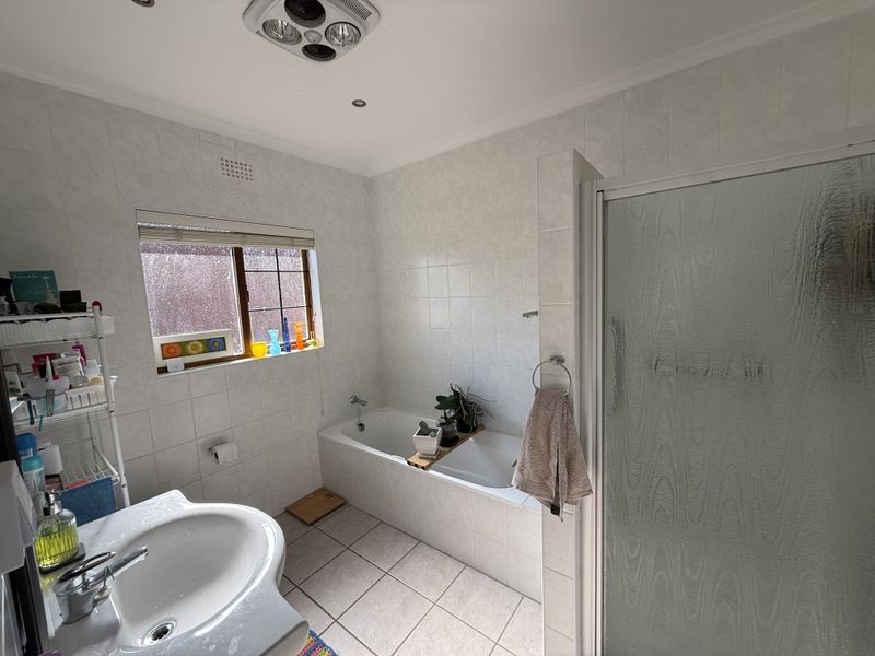 A functional bathroom featuring a built-in bathtub, separate shower enclosure, and pedestal basin with neutral wall and floor tiling.