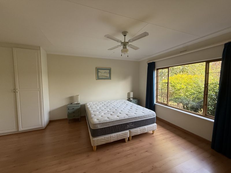 Spacious bedroom featuring laminate flooring, a built-in wardrobe, ceiling fan, and a large window overlooking the garden.