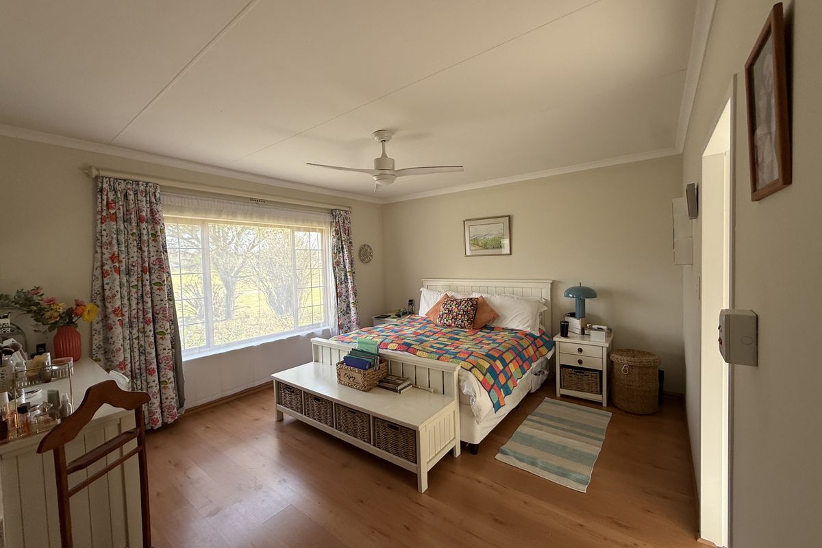A well-maintained bedroom featuring laminate flooring, a ceiling fan, and a large window providing natural light.