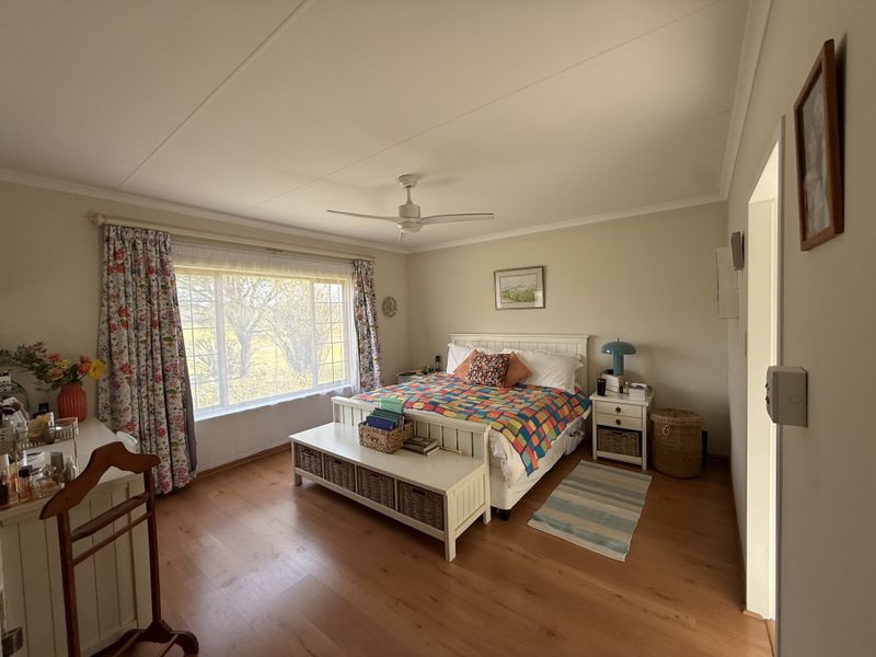 A well-maintained bedroom featuring laminate flooring, a ceiling fan, and a large window providing natural light.