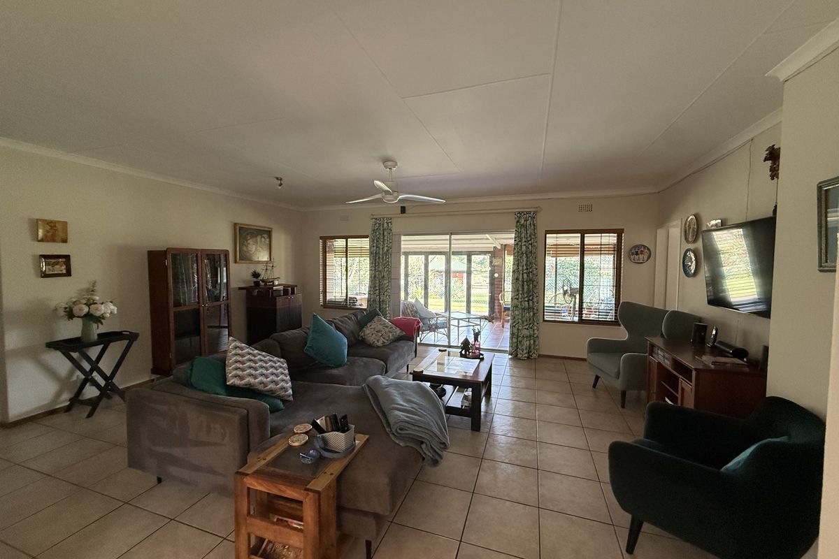 Spacious living room featuring neutral tiled flooring, a ceiling fan, and large sliding glass doors providing natural light and access to the outdoor patio area.