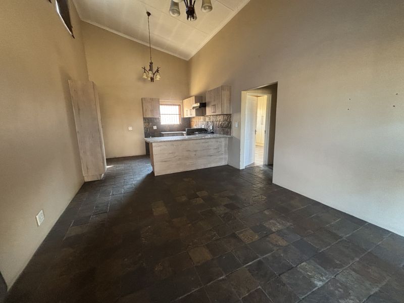 Spacious open-plan living and kitchen area featuring vaulted ceilings, tiled flooring, and modern wood-finish cabinetry with a breakfast counter.