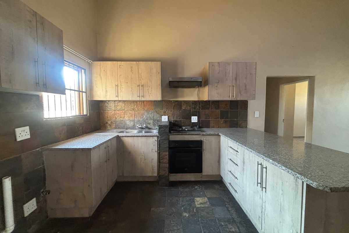 A functional kitchen featuring light wood cabinetry, granite countertops, built-in oven, gas hob, and a tiled splashback with a breakfast bar area.