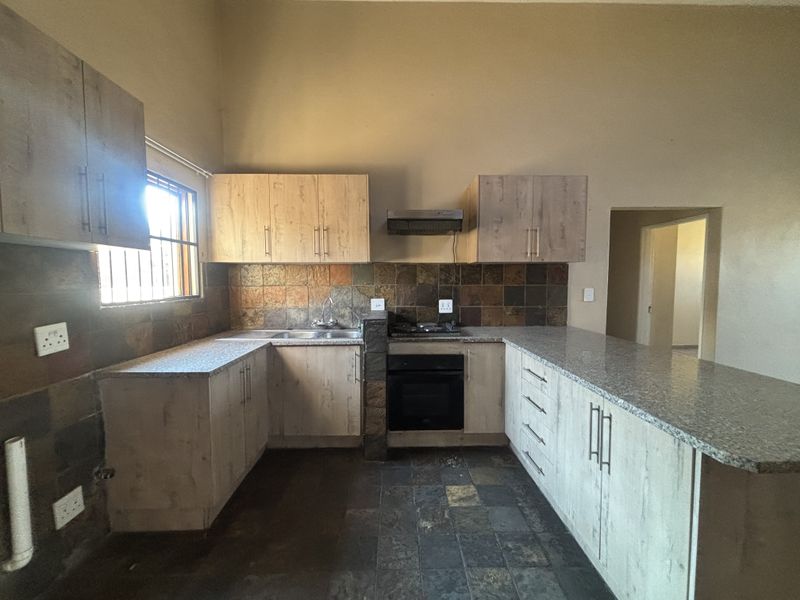 A functional kitchen featuring light wood cabinetry, granite countertops, built-in oven, gas hob, and a tiled splashback with a breakfast bar area.