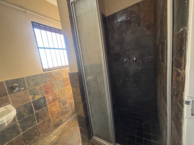 A bathroom featuring a shower enclosure with dark slate tiling, a wall-mounted basin, and a window with security bars.