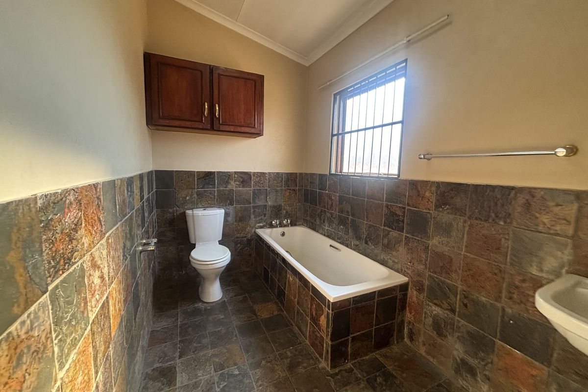A functional bathroom featuring a built-in bathtub, toilet, and wall-mounted storage cabinet, finished with rustic slate-style wall and floor tiles.