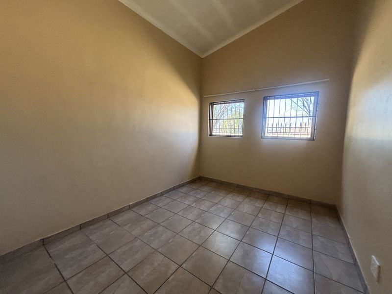An empty bedroom featuring tiled flooring, vaulted ceilings, and windows fitted with security bars.