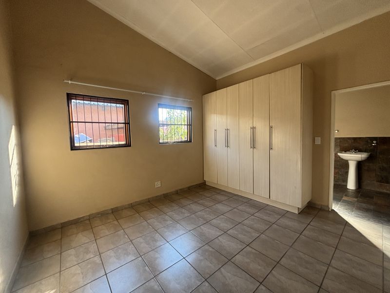 A spacious bedroom featuring vaulted ceilings, tiled flooring, and ample built-in cupboard storage, with an adjoining en-suite bathroom area.