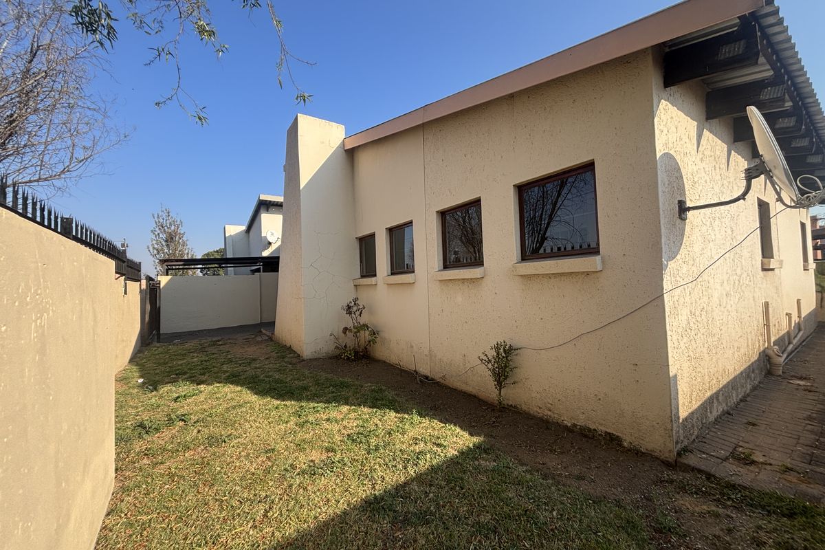 Rear exterior view of the townhouse featuring a small garden, paved walkway, and perimeter wall with security spikes.