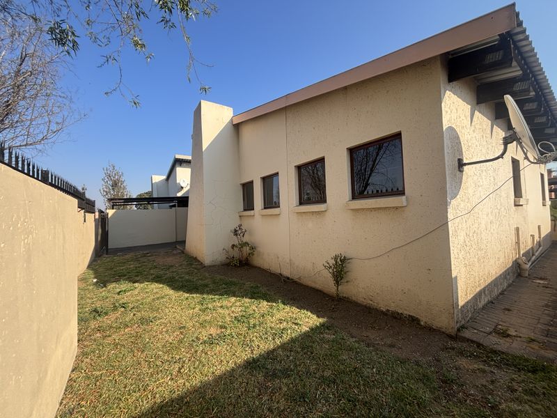 Rear exterior view of the townhouse featuring a small garden, paved walkway, and perimeter wall with security spikes.