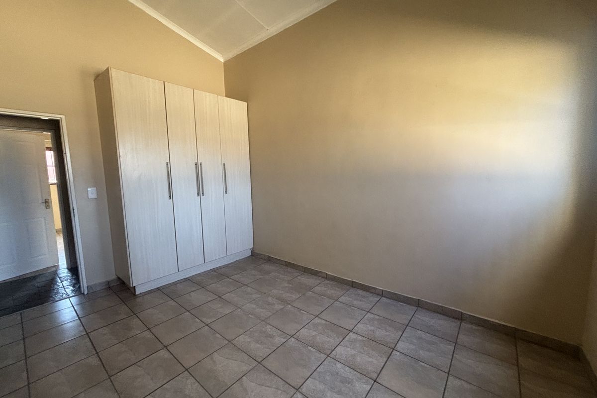 A clean, empty bedroom featuring tiled flooring, a vaulted ceiling, and built-in cupboards, offering a neutral space ready for personalization.