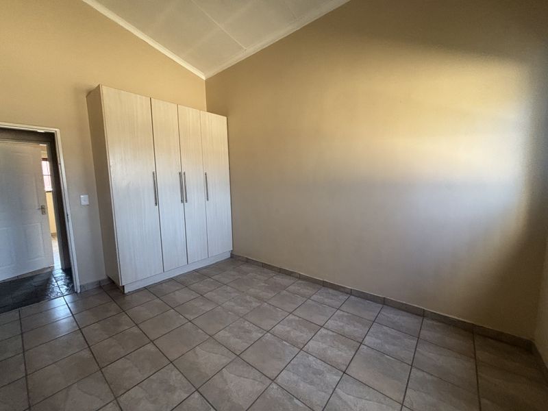 A clean, empty bedroom featuring tiled flooring, a vaulted ceiling, and built-in cupboards, offering a neutral space ready for personalization.