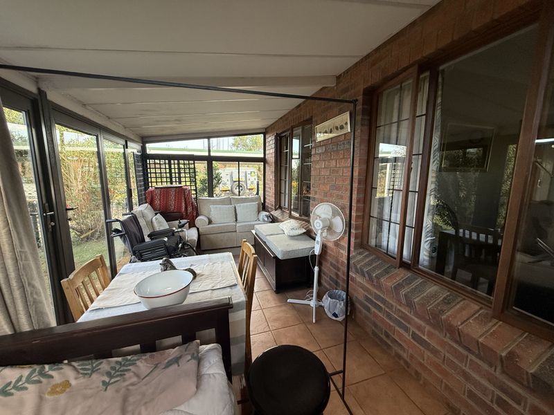 A covered patio area featuring exposed brick walls, tiled flooring, and large windows, providing a versatile space for outdoor relaxation and dining.