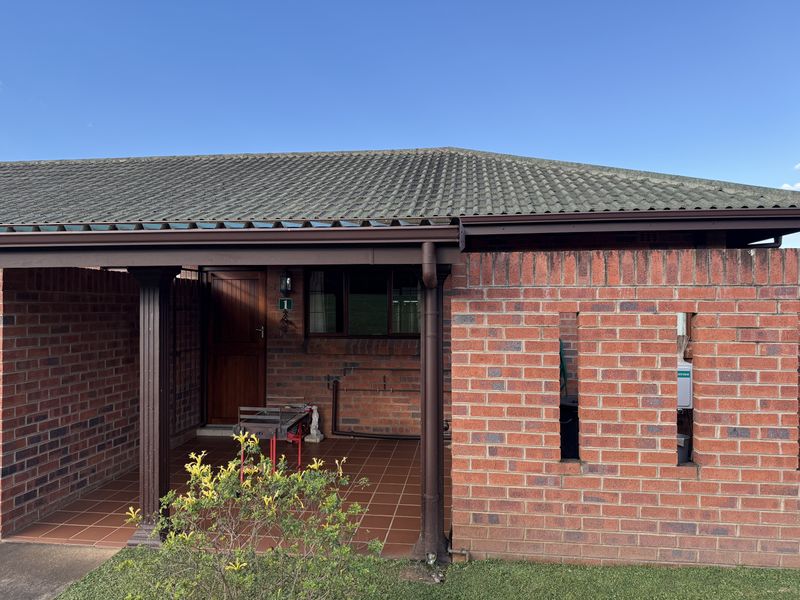 A covered outdoor patio area featuring exposed brick walls, tiled flooring, and a timber entrance door, providing a functional sheltered space.
