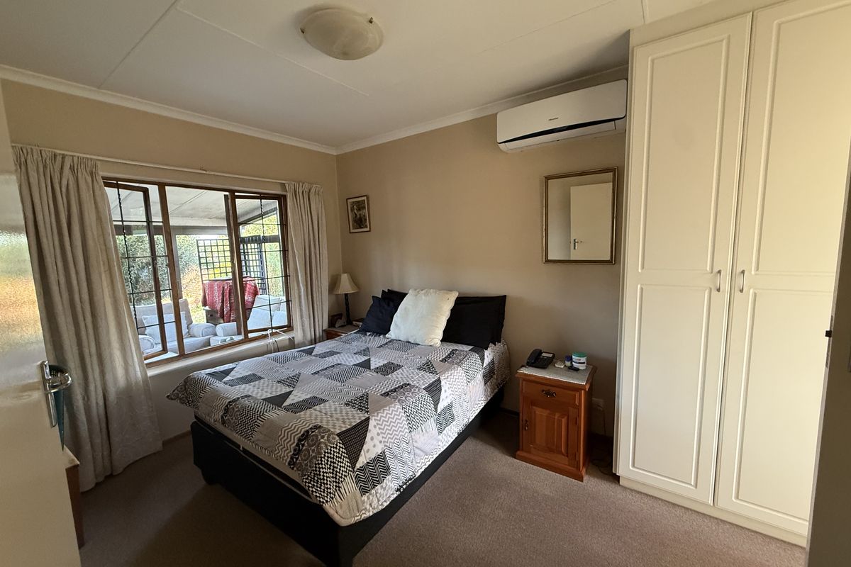A functional bedroom featuring built-in wardrobes, carpeted flooring, and a wall-mounted split-system air conditioner, with natural light from a large window.