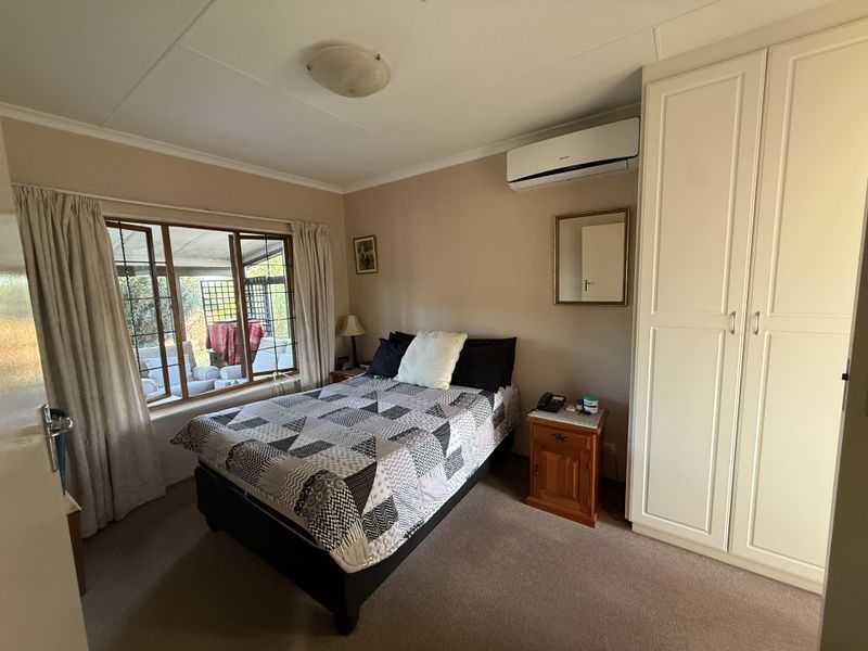 A functional bedroom featuring built-in wardrobes, carpeted flooring, and a wall-mounted split-system air conditioner, with natural light from a large window.
