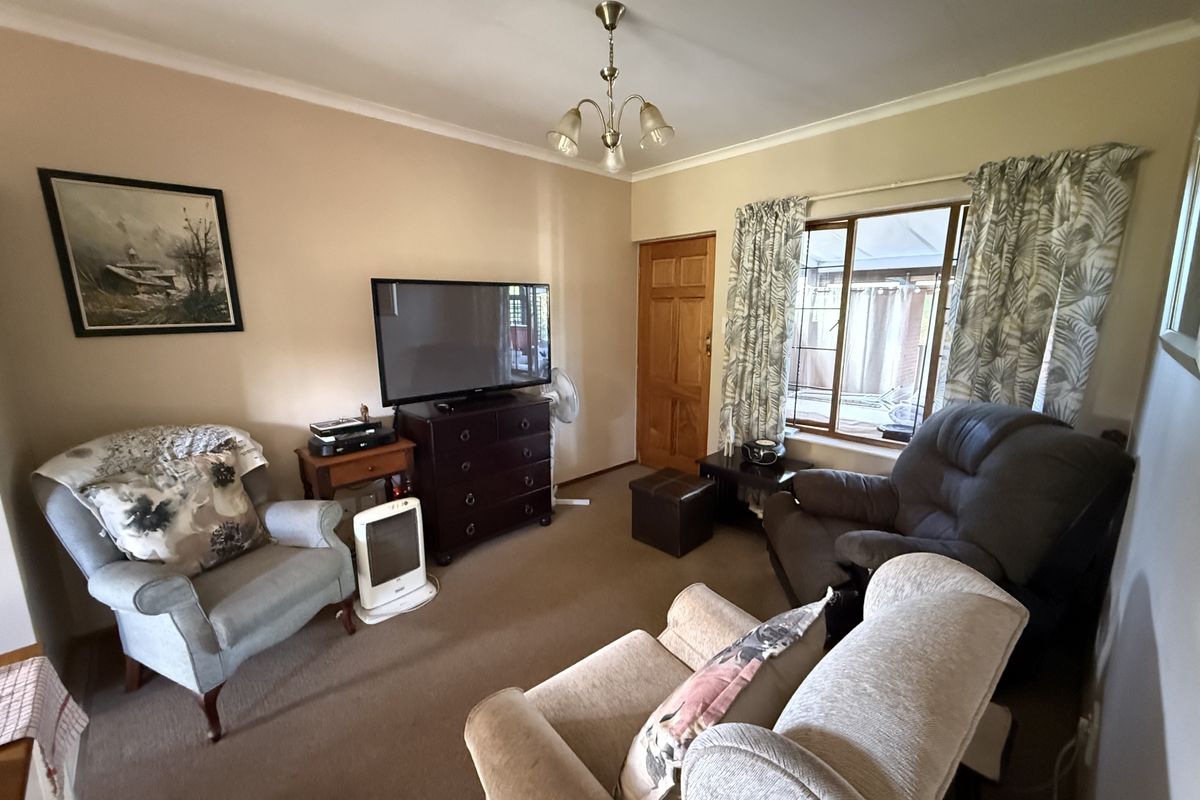 A cozy living room featuring neutral wall tones, carpeted flooring, and a window providing natural light.