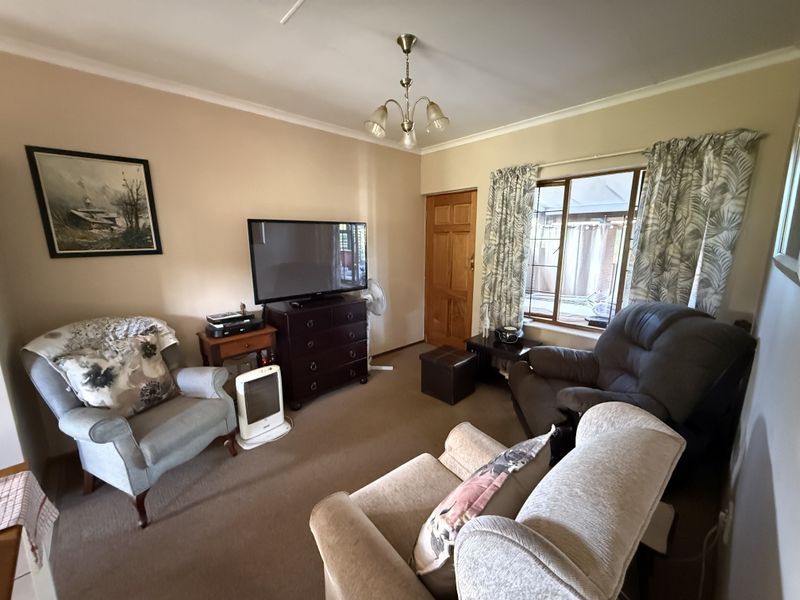 A cozy living room featuring neutral wall tones, carpeted flooring, and a window providing natural light.