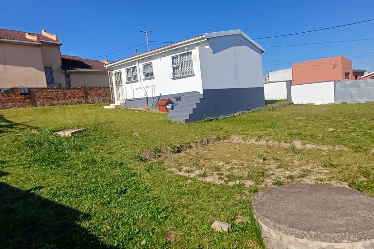 Rear view of the property featuring a spacious garden, brick boundary walls, and a small detached structure with security bars on windows.