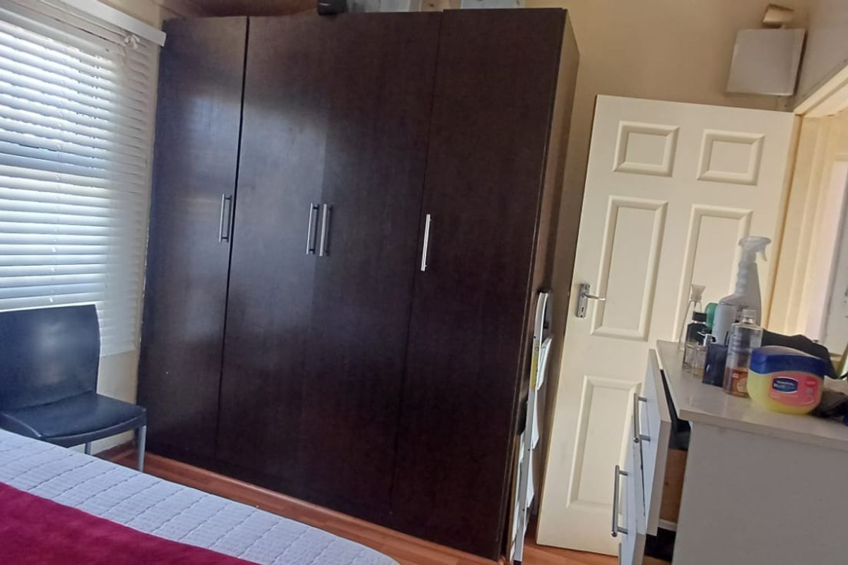 A bedroom featuring laminate flooring, a large dark wood built-in wardrobe, and venetian blinds on the window.
