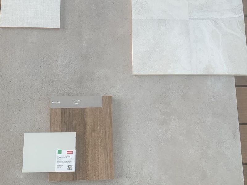 A collection of material samples including stone-look tiles, wood-grain laminate, and textile swatches for interior design planning.