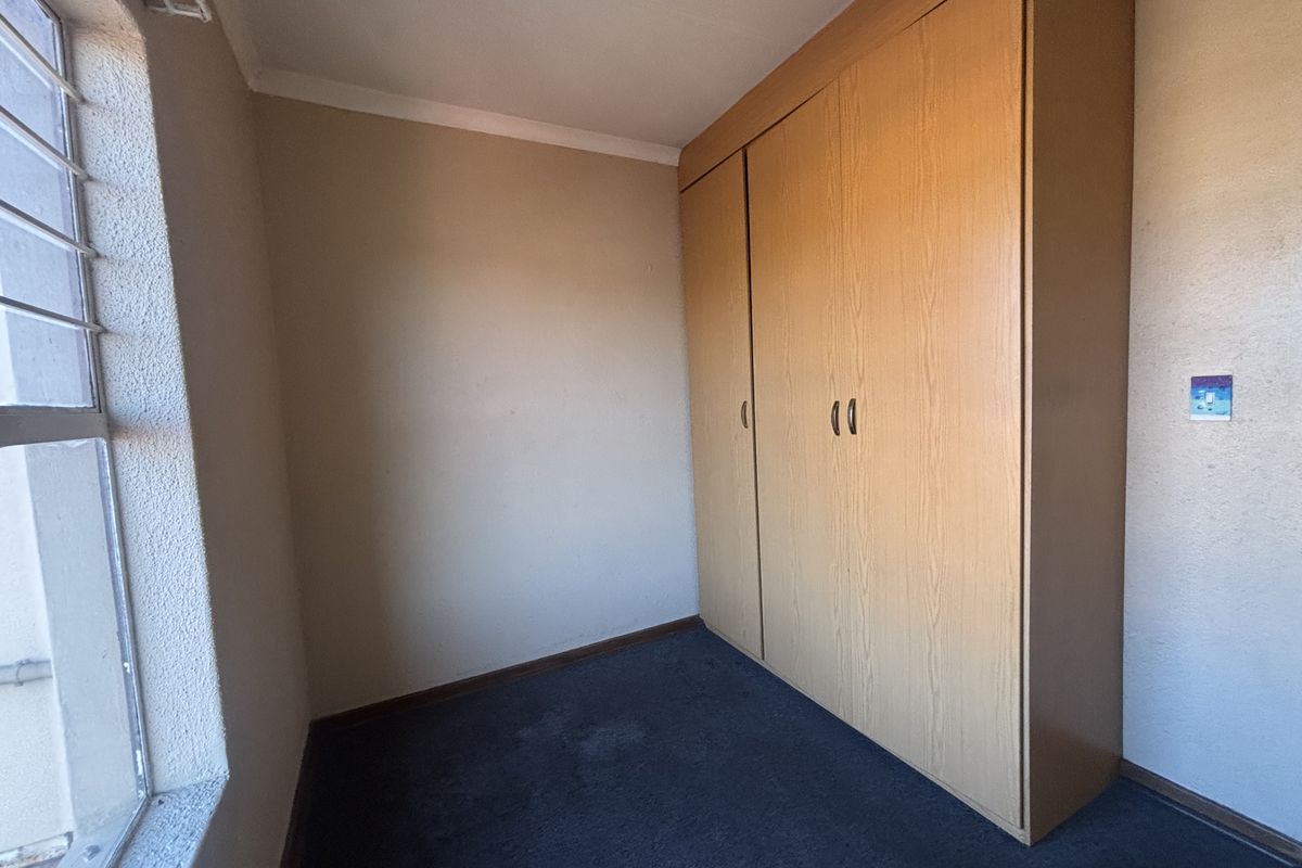 An empty bedroom featuring a built-in wooden wardrobe, carpeted flooring, and a window with security bars.