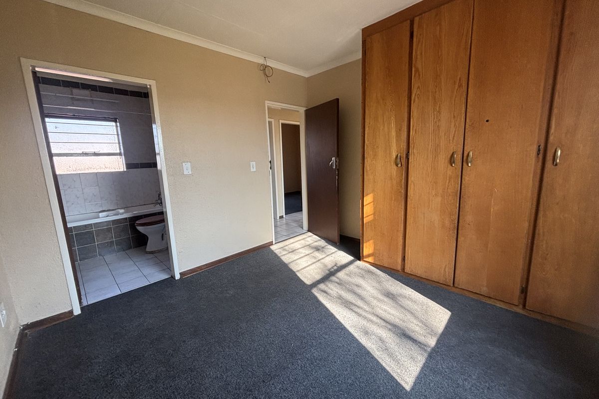 An empty bedroom featuring built-in wooden cupboards, carpeted flooring, and direct access to an en-suite bathroom.
